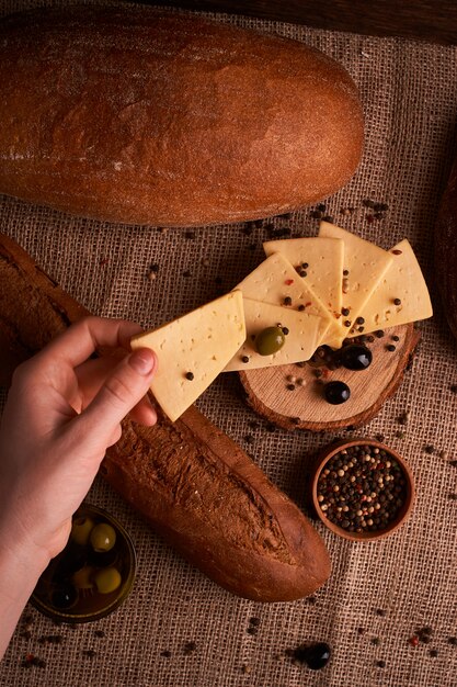 Woman hold slice of Traditional Dutch semi hard cheese on Olives, bread and baguette.