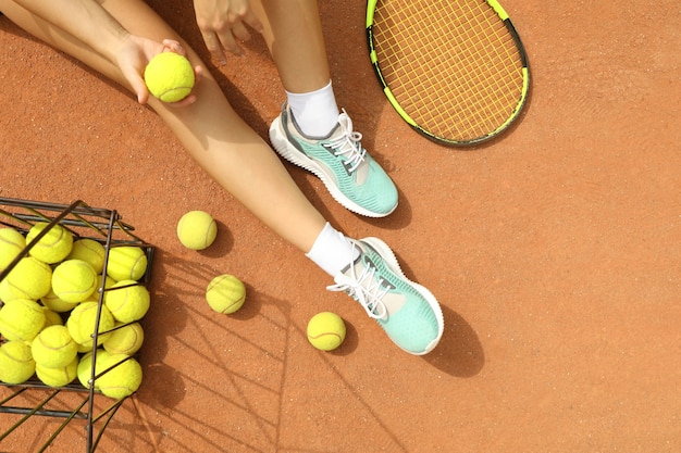 Woman hold tennis ball on clay court with racket and balls