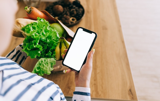 Женщина держит смартфон с белым экраном, макет. концепция рынка продуктов питания онлайн.