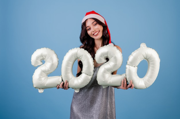 Woman holding 2020 new year balloons wearing christmas hat and dress