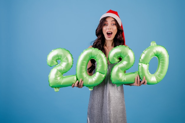 Woman holding 2020 new year balloons wearing christmas hat and dress