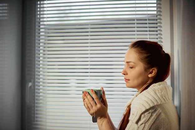 Фото Женщина, держащая чашку чая и пьющая, сидя у окна.