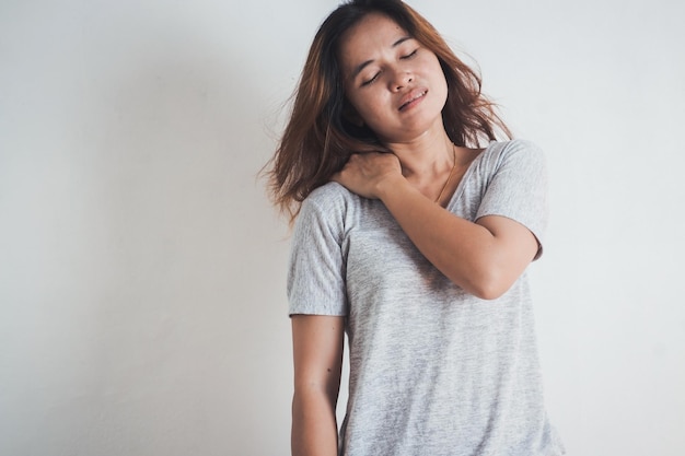 白い背景に立って肩を痛めている女性