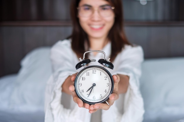 Woman holding alarm clock on bed happy female wake up in the morning daily routine sleep relaxing and have a nice day concepts