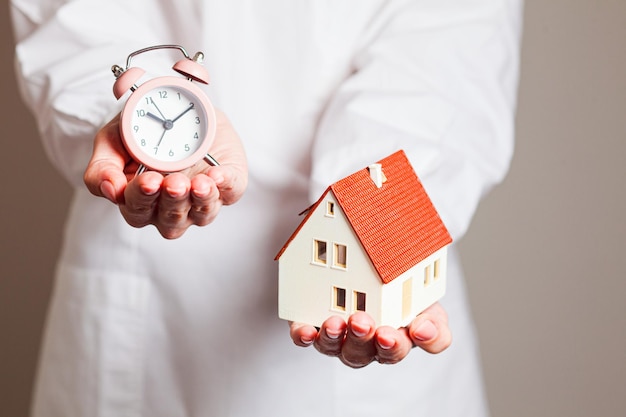 Woman holding alarm clock and mockup house