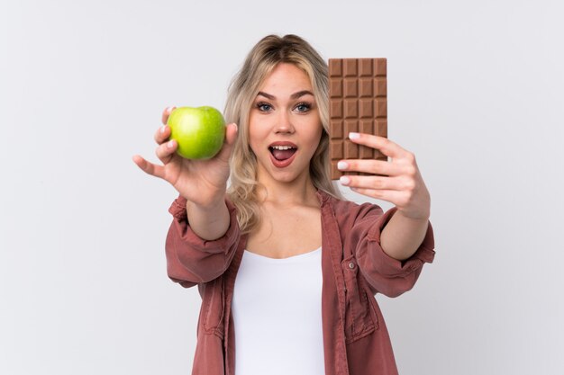 Woman holding apple an chocolate over isolated wall