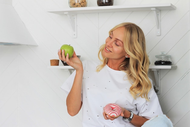 Woman holding apple and donut in her hands in healthy fruit versus sweet junk food temptation in fitness