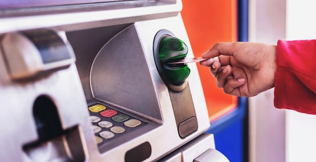 Woman holding an ATM card withdrawing cash from an ATM