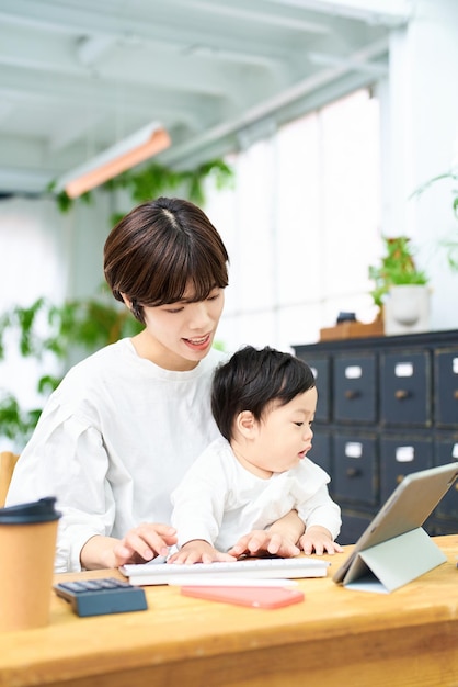 A woman holding a baby and operating a computer indoors