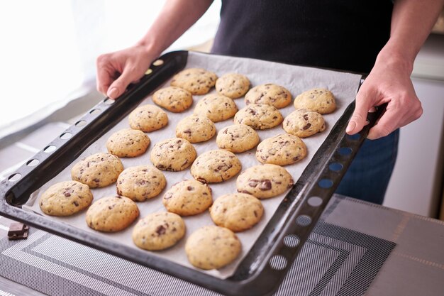 Woman holding baking tray full of freshly made Chocolate chip cookies