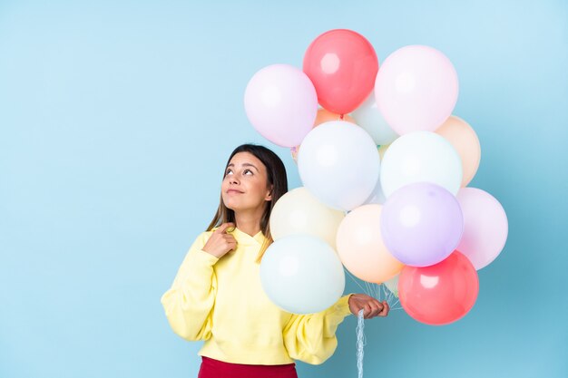 Woman holding balloons in a party over blue wall thinking an idea