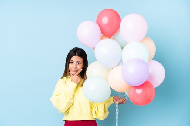 Woman holding balloons in a party over blue wall thinking an idea