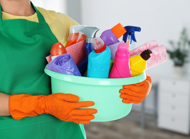 Woman holding basin with cleaning supplies in office closeup