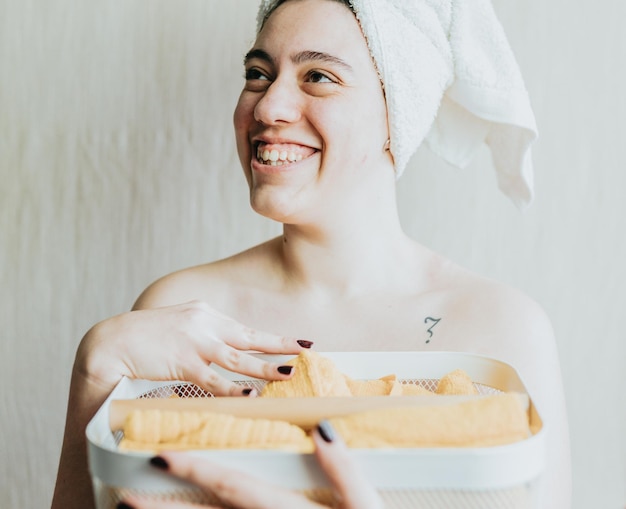 다른 샤워 용품이 있는 바구니를 들고 있는 여성 밝은 노란색과 돌돌 말린 수건을 손에 들고 있는 여성 금속 메쉬 수납 흰색 바구니 편안한 목욕을 위한 제품 준비