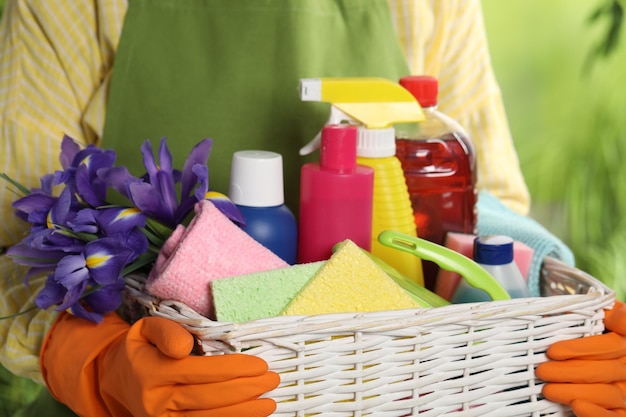 Woman holding basket with spring flowers and cleaning supplies outdoors closeup