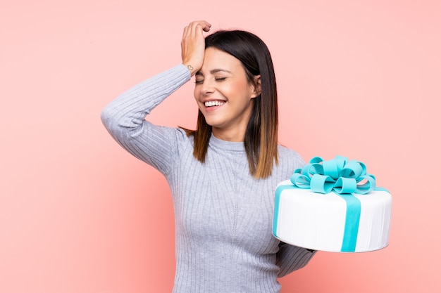 Woman holding a big cake over pink wall has realized something and intending the solution