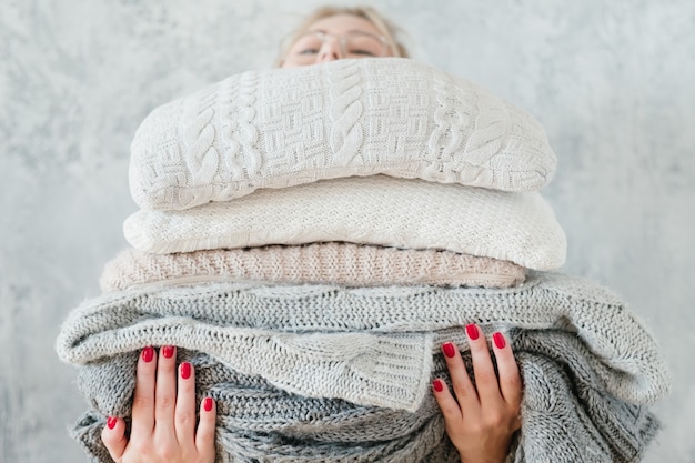 Donna che mantiene grande pila di plaid e coperte lavorate a maglia. arredamento per la casa invernale accogliente e caldo