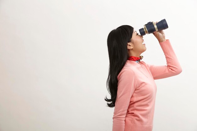 Woman holding binoculars while standing against white background