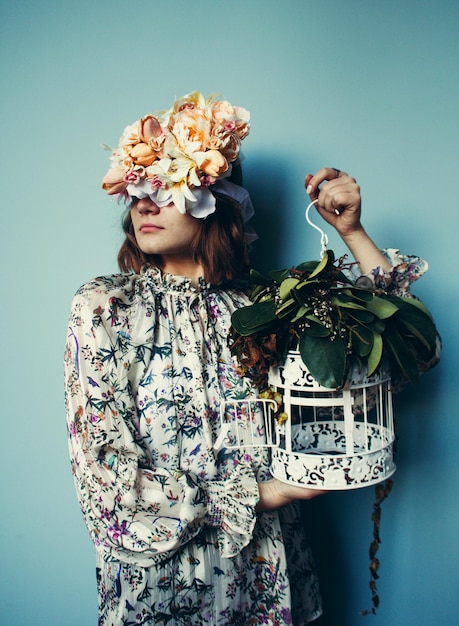 Photo woman holding birdcage while standing against blue wall