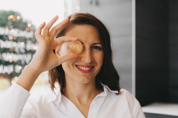 Woman holding bitcoin in front of her eye. Beauty woman head with money bitcoin in her eye. bitcoin cryptocurrency.