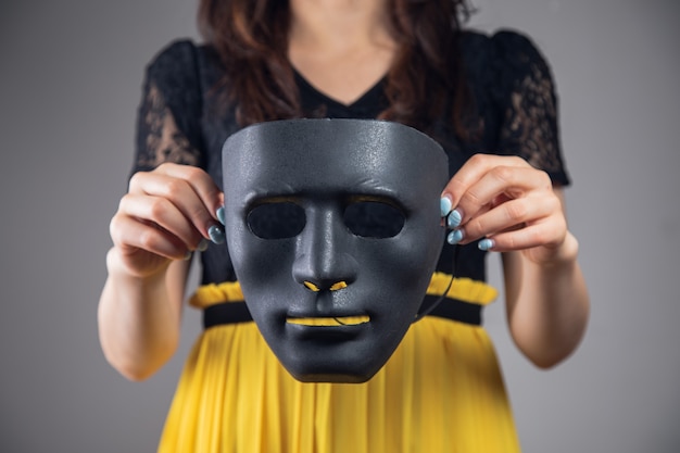 Photo woman holding black plastic mask on gray background