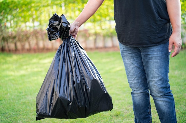 Photo woman holding black plastic trash bin bags of garbage on the pavement, clean environment concept.