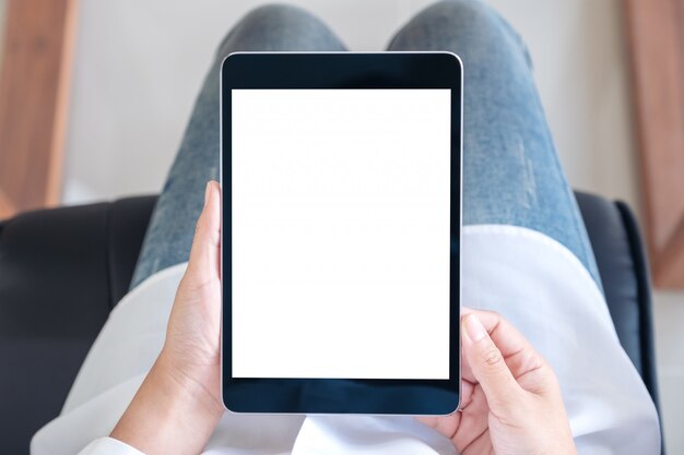 Woman holding black tablet pc with blank white screen while sitting on a chair