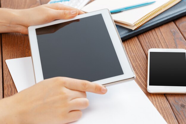 Woman holding blank tablet device over a wooden workspace table