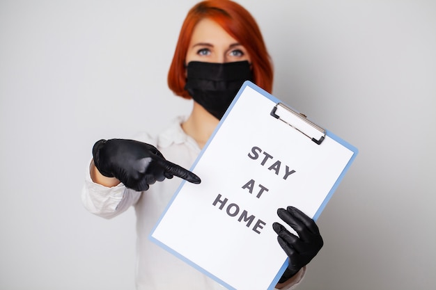 Женщина, держащая бланк с надписью остаться дома, призывает прекратить распространение covid-19