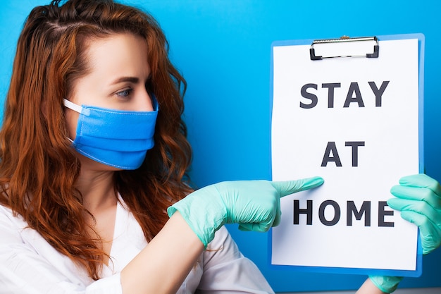 Woman holding blank with inscription stay at home calling for stop spreading covid-19