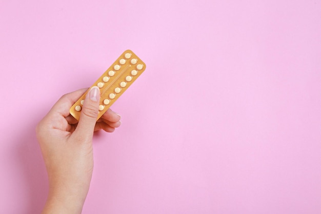 Foto donna che tiene blister con pillole anticoncezionali su sfondo rosa vista dall'alto spazio per il testo