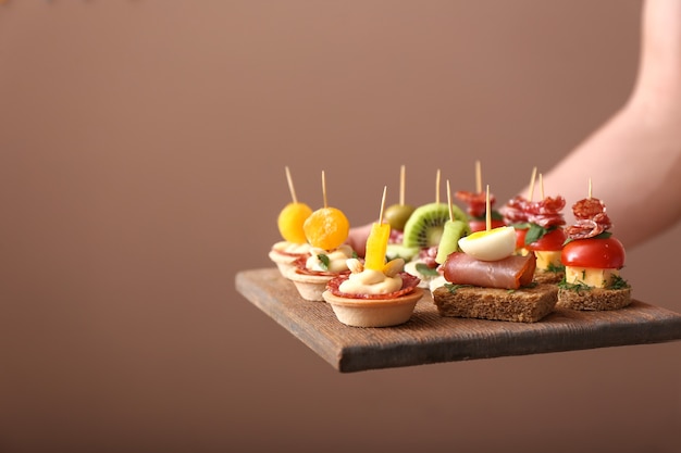 Photo woman holding board with tasty canapes on brown