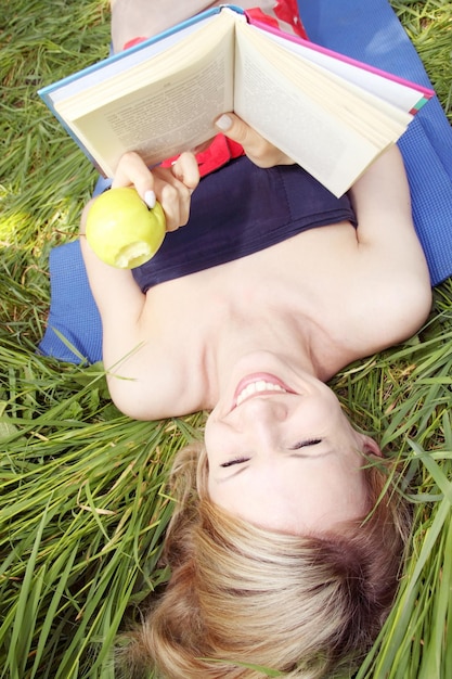 Женщина держит книгу и ест яблоко