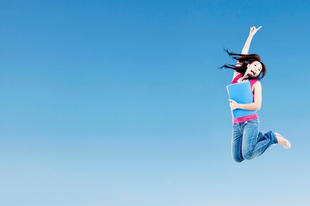 Photo woman holding book while jumping against blue sky