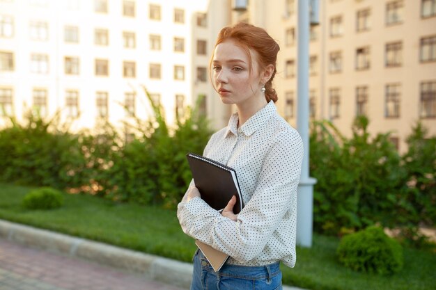 Фото Женщина с книгой в руках, стоя в кампусе