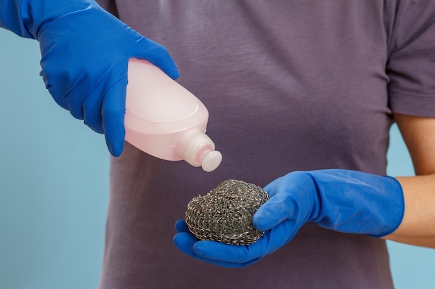 Woman holding a bottle of dishwashing liquid and a sponge on a blue background