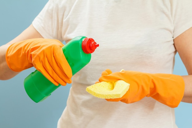 Woman holding a bottle of dishwashing liquid and a sponge on a blue background