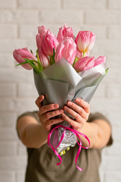 Женщина, держащая букет красивых розовых весенних тюльпанов возле белой кирпичной стены.