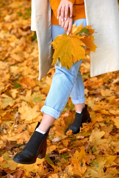 Woman holding a bouquet of leaves and kicks leaves by foot in park. shallow depth of field vertical photo