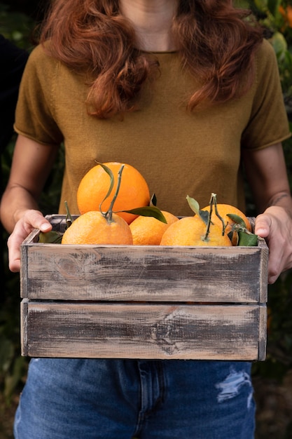 Photo woman holding a box full of oranges in her hands