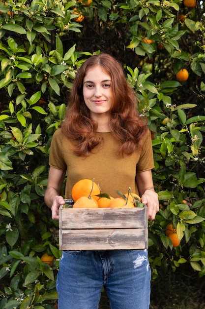 Photo woman holding a box full of oranges in her hands