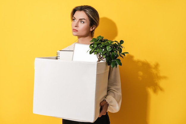 Woman holding box with personal items after job resignation against yellow background