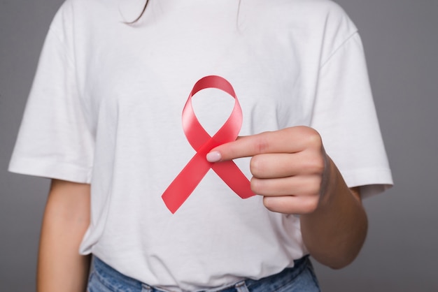 Woman holding breast with pink ribbon over white wall. Concept photo to support breast cancer cause. PS: you can change the pink ribbon into red for AIDS support cause.