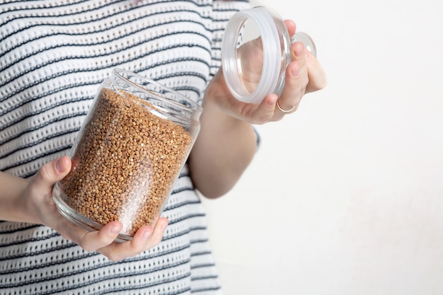 Woman holding buckwheat in glass jar for storage. Empty space