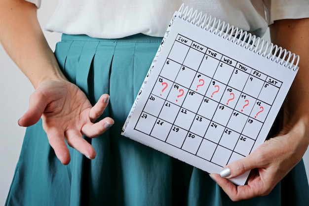 Calendario della holding della donna con il periodo mancato segnato. gravidanza indesiderata, salute della donna e ritardo delle mestruazioni.