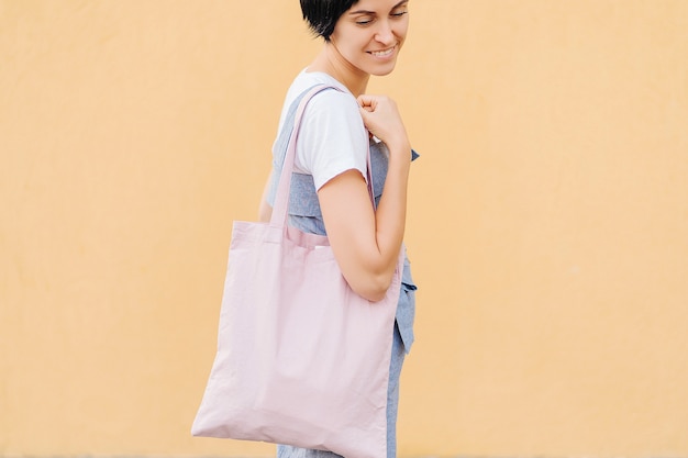 Woman holding canvas tote bag on yellow background. Reusable eco bag. 