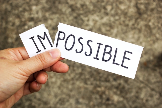 Woman holding a card with text Impossible over cement background