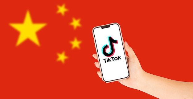 背景に中国国旗が消光しているTikTokのロゴを掲げた携帯電話を握っている女性