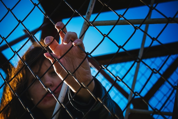 Photo woman holding chainlink fence against clear blue sky