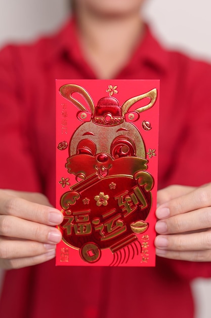 写真 金色のウサギと幸せな旧正月の休日のための祝福の言葉のお金の贈り物を持つ中国の赤い封筒を保持している女性